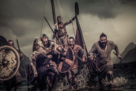 The battle of maldon Warriors in Viking attire emerge from a stormy sea, wielding shields and weapons, as a longship looms in the background.