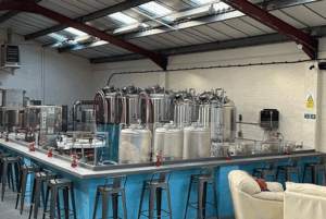 A modern brewery interior featuring stainless steel tanks, bar seating, and a cozy lounge area with bright lighting and vibrant decor.