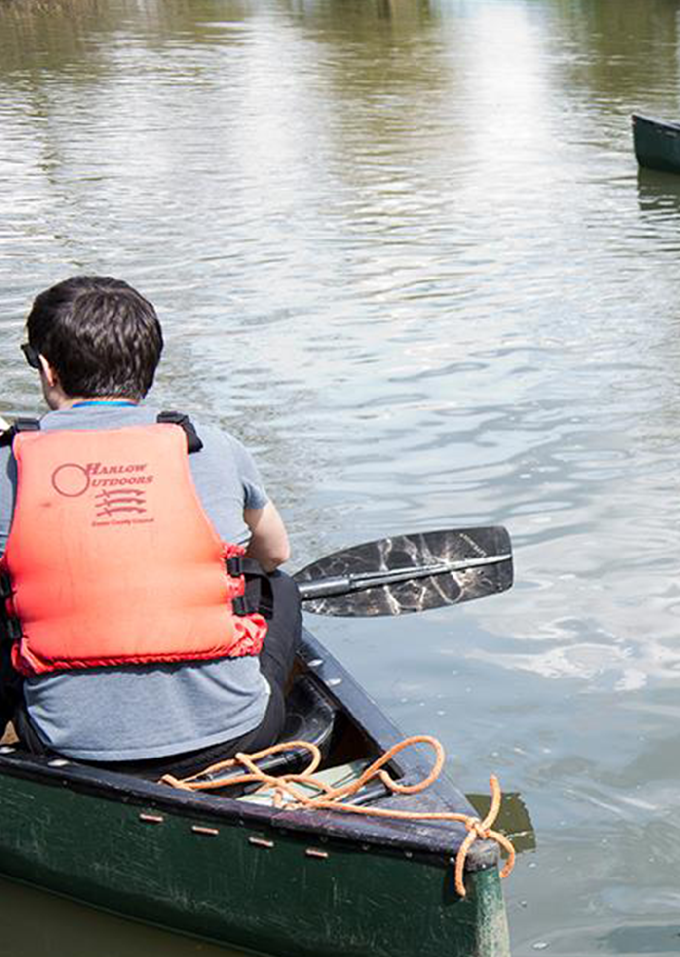 A person in a red life jacket paddles a canoe on a calm river, enjoying a sunny day outdoors.