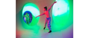 A room filled with vibrant lights, someone dancing and someone playing the flute.